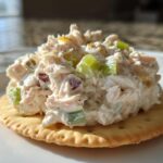Close-up of a scoop of creamy ham salad recipe with celery pieces served on a round butter cracker.