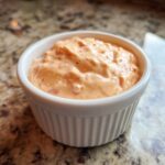 Close-up of creamy, orange-tinted big mac sauce with visible relish pieces in a small white bowl.
