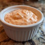 Close-up of creamy, orange-pink homemade big mac sauce served in a small white fluted ramekin.