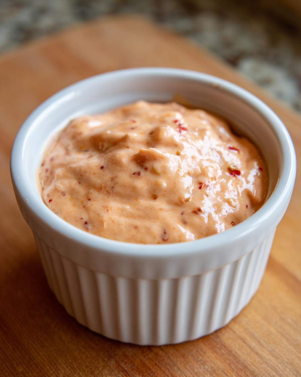 A close-up of creamy, orange-hued big mac sauce with visible relish pieces served in a small white ramekin.