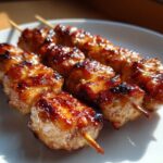Close-up of three skewers featuring juicy, glazed, and slightly charred chicken skewers on a white plate.