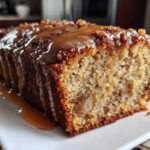 Close-up of a moist slice of apple dapple cake drizzled heavily with caramel sauce on a white plate.