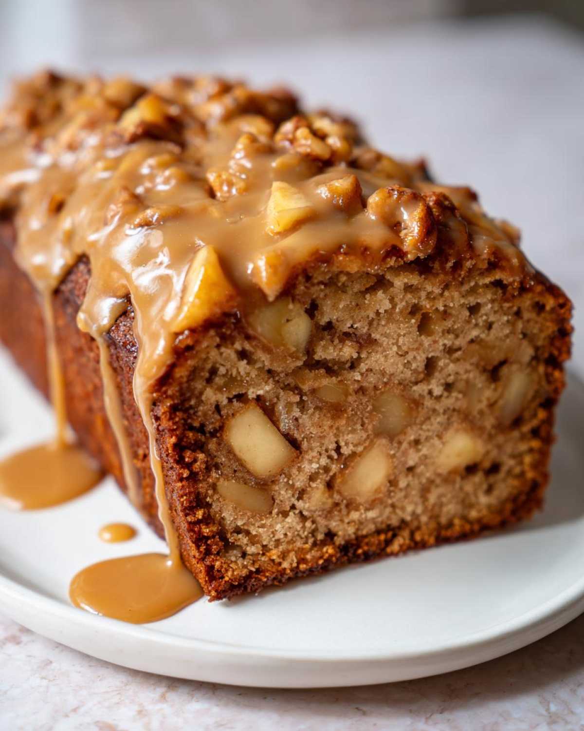 Close-up of a slice of moist apple dapple cake topped with thick caramel sauce and walnuts.