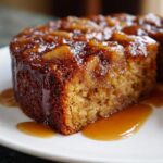 Close-up of a moist slice of apple dapple cake topped with caramelized apples and drizzled with caramel sauce.