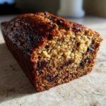 A close-up, cross-section view of a moist slice of vegan banana bread studded with chocolate chips.