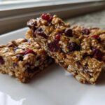 Two chewy no bake granola bars packed with oats, dried cranberries, and chocolate chips on a white plate.