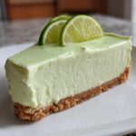 A perfect slice of creamy, light green no-bake key lime cheesecake on a white plate, topped with lime slices.