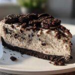 A decadent slice of creamy Oreo cheesecake with a dark chocolate crust and topped with crushed Oreos.