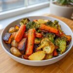 A white bowl filled with perfectly caramelized roasted vegetables, including carrots, potatoes, and broccoli, seasoned with herbs.