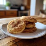 A stack of four soft, chewy snickerdoodles generously coated in cinnamon sugar, resting on a white plate.