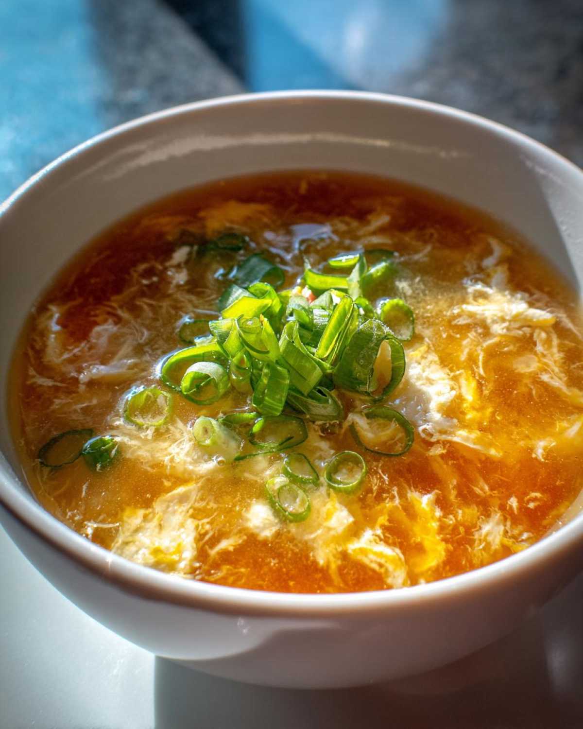 A close-up of a bowl of savory egg drop soup, garnished with fresh green onions.