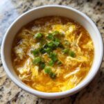 Close-up of a bowl of hot egg drop soup garnished with fresh green onions.