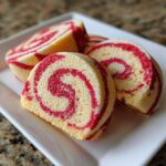 Three slices of red and white swirl pinwheel cookies arranged on a white rectangular plate.