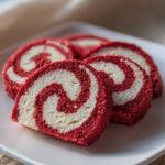 Four slices of vibrant red and white swirled pinwheel cookies arranged on a white plate.