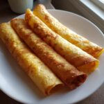 Four golden, rolled tortillas ready to be filled for potato tacos, resting on a white plate.