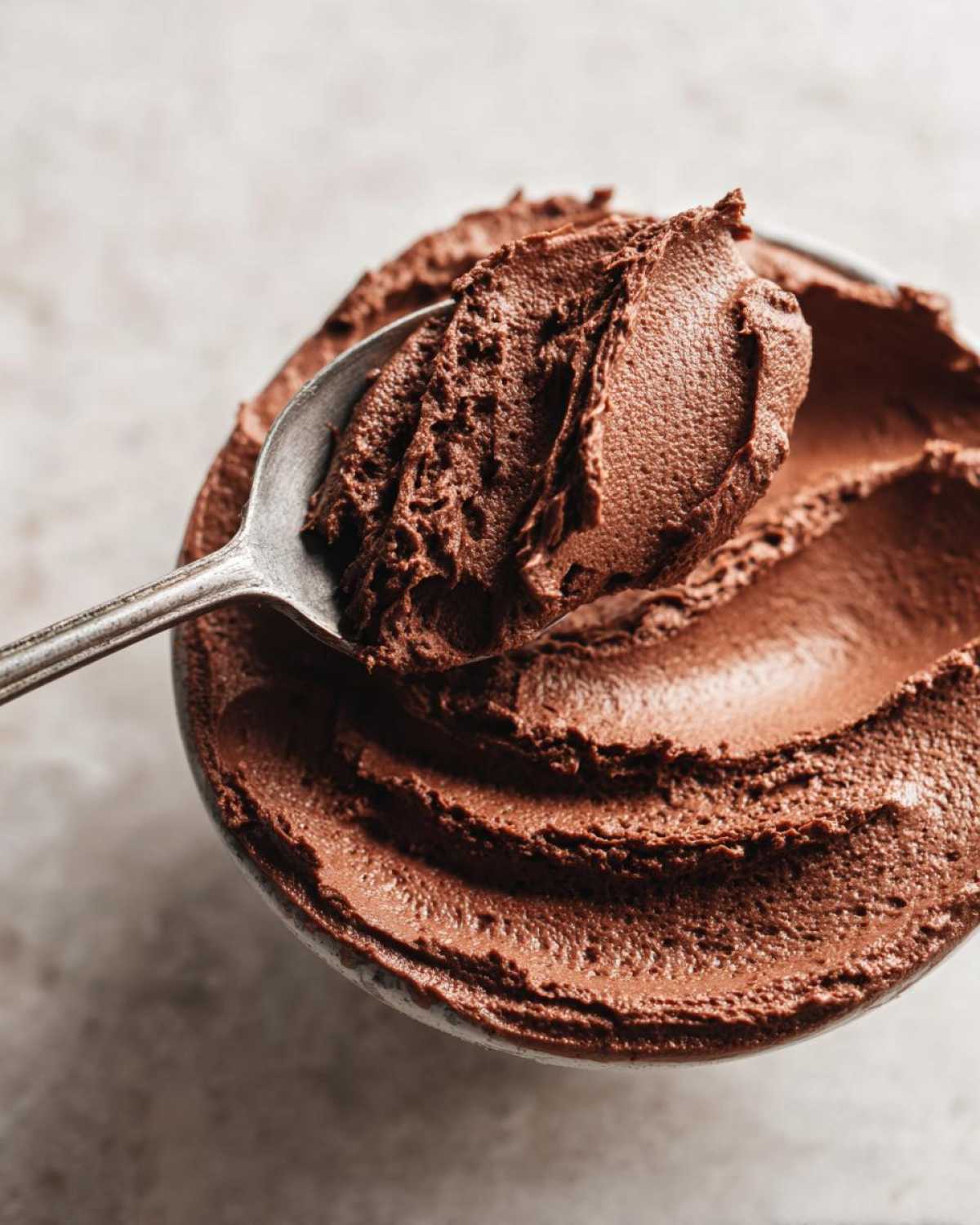 Close-up of a spoonful of rich, dark chocolate mousse being lifted from a bowl.