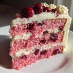 A perfect slice of pink layer Cherry Cake showing layers of pink sponge, white cream, and whole cherries, topped with fresh cherries.