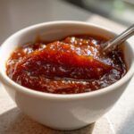 Close-up of rich, dark brown pear butter served in a small white bowl with a spoon resting inside.
