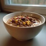 A close-up of a steaming white bowl filled with rich cowboy soup featuring ground beef, kidney beans, and corn.