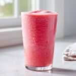 A tall glass filled with a frosty, bright pink watermelon smoothie, showing condensation on the outside.
