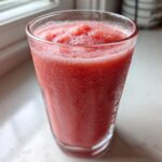 A close-up of a frosty, bright pink watermelon smoothie served in a tall glass.