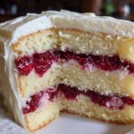 Close-up of a slice of white chocolate raspberry cake showing three layers of vanilla cake and raspberry filling.
