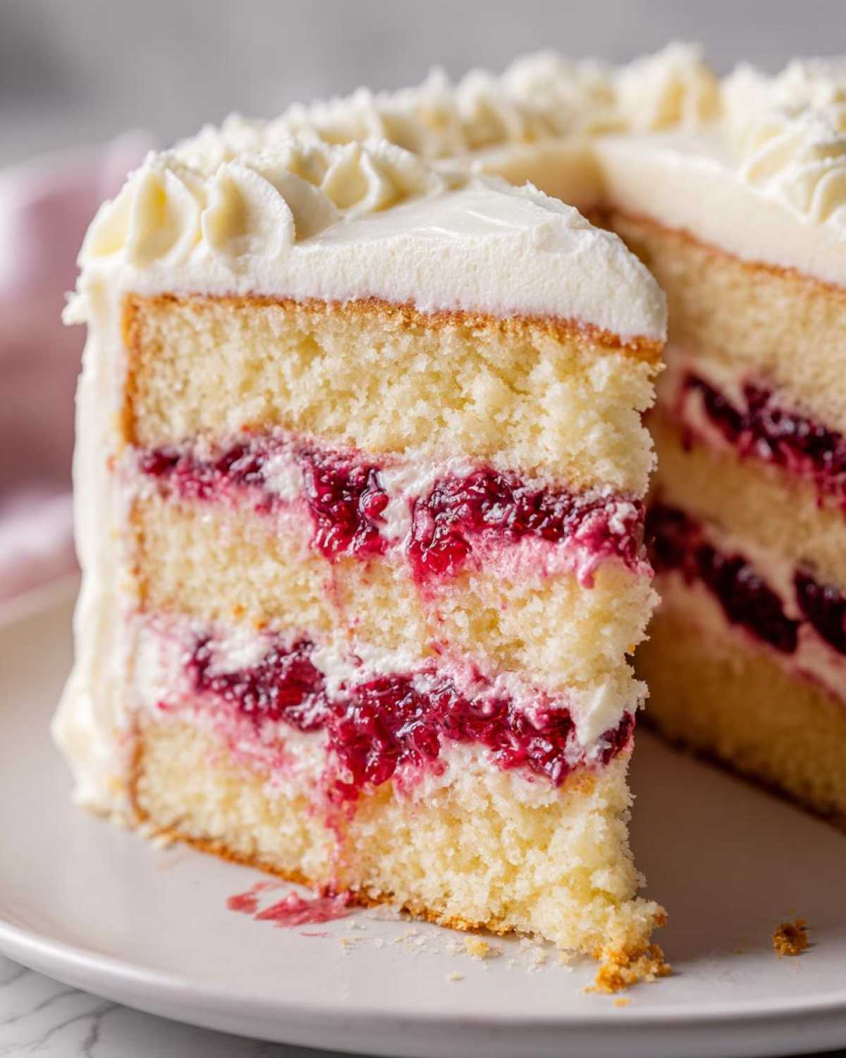Close-up of a slice of white chocolate raspberry cake showing layers of white cake, raspberry filling, and white frosting.