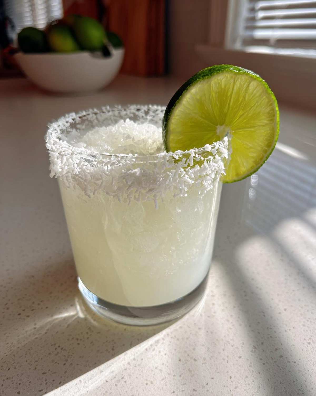 Close-up of a frosty white christmas margarita with a coconut-rimmed glass and a lime wheel garnish.