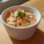 Close-up of bright orange remoulade sauce topped with fresh parsley and chopped onions in a white bowl.