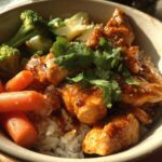 A close-up of 15-Minute Saucy Chicken Satay Bowls featuring saucy chicken pieces over rice with carrots, broccoli, and cilantro.