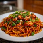 A close-up of 20-Minute Saucy Gochujang Chicken Noodles topped with green onions and sesame seeds.