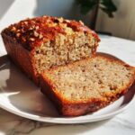 A loaf of Air Fryer Banana Bread with Pecans, with one thick slice cut and resting next to the main loaf on a white plate.