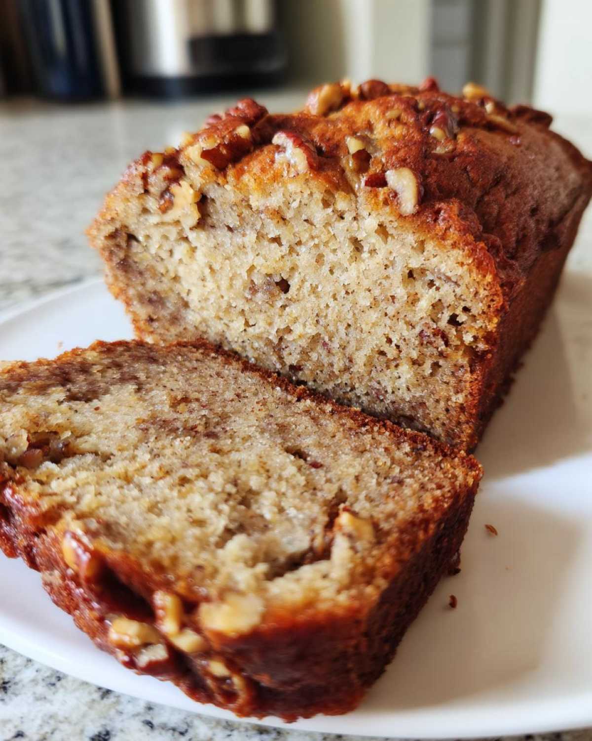 Close-up of a loaf of Air Fryer Banana Bread with Pecans, showing a thick slice cut and revealing the moist interior texture.