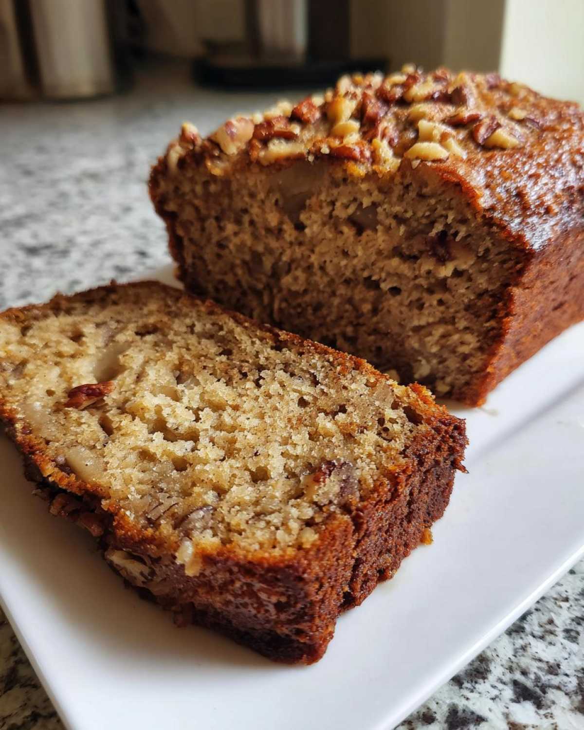 A slice of moist Air Fryer Banana Bread with Pecans next to the main loaf, showing the texture and topping.
