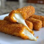 Close-up of golden brown Air Fryer Mozzarella Sticks with melted cheese stretching out from a broken stick.