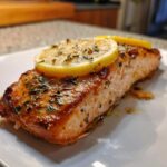 Close-up of a perfectly cooked Air Fryer Salmon Fillets with Lemon, topped with a lemon slice and herbs.