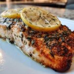 Close-up of a perfectly cooked Air Fryer Salmon Fillets with Lemon, seasoned with herbs and topped with lemon slices.