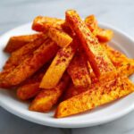A close-up of bright orange Air Fryer Sweet Potato Fries with Cajun Spice piled on a white plate.