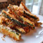 A close-up of golden brown Air Fryer Zucchini Fries with Panko stacked on a white plate.