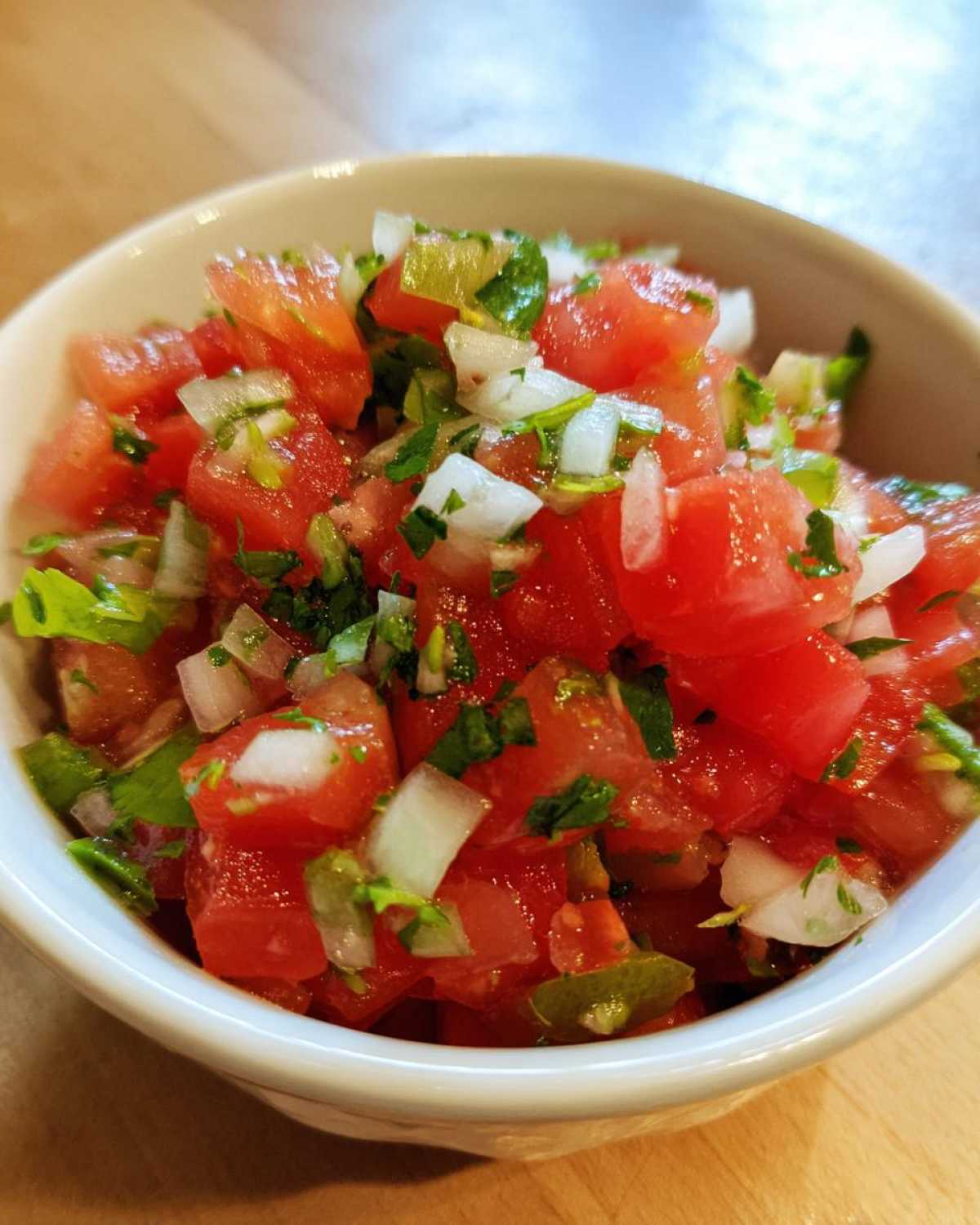 Close-up of a white bowl filled with freshly chopped tomatoes, onions, and cilantro for Authentic Pico de Gallo with Lime.