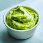 A close-up of thick, bright green Avocado Crema with Lime and Cilantro swirled in a small white ramekin.