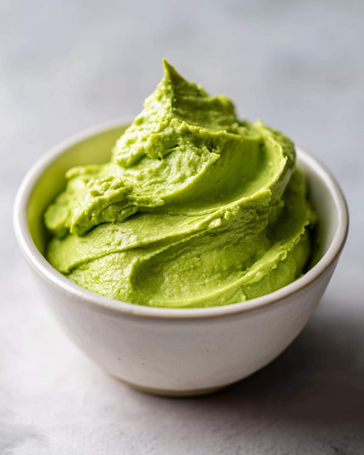 A close-up of vibrant green, perfectly piped Avocado Crema with Lime and Cilantro in a small white bowl.