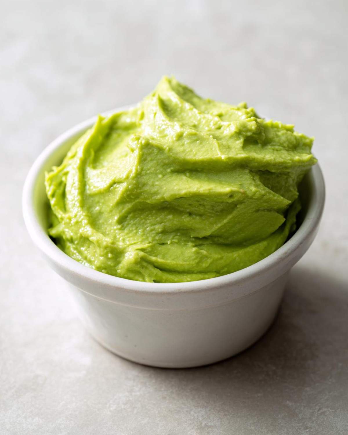 A small white bowl filled with vibrant, smooth Avocado Crema with Lime and Cilantro.