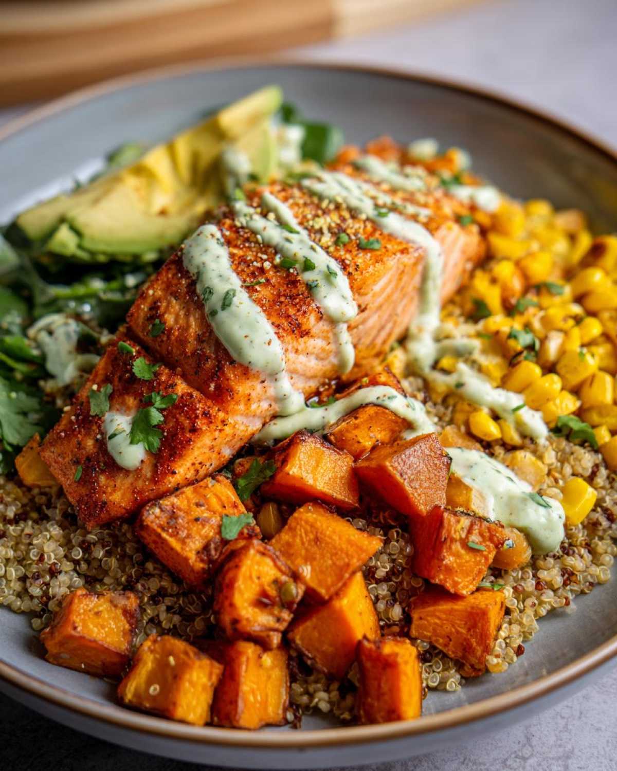 Close-up of a BBQ Salmon Bowls with Sweet Potato featuring a seasoned salmon fillet over quinoa, roasted sweet potatoes, corn, and avocado.