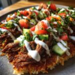 Close-up of a serving of Beef Shawarma Crispy Rice Salad topped with shredded beef, fresh vegetables, and white sauce.