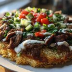 A plate featuring Beef Shawarma Crispy Rice Salad with seasoned beef, crispy rice base, fresh tomatoes, cucumbers, and a white sauce drizzle.