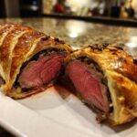 Cross-section of a golden-brown Beef Wellington Individual Servings showing medium-rare pink beef tenderloin inside flaky pastry.