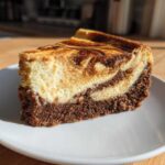A tempting slice of Biscoff Greek Yogurt Cheesecake Hack showing a dark crust and a creamy, swirled Biscoff topping.