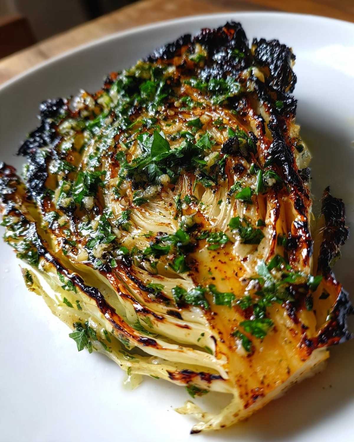 Close-up of a Blistered Cabbage Steak, charred edges, drizzled with garlic butter and fresh parsley.