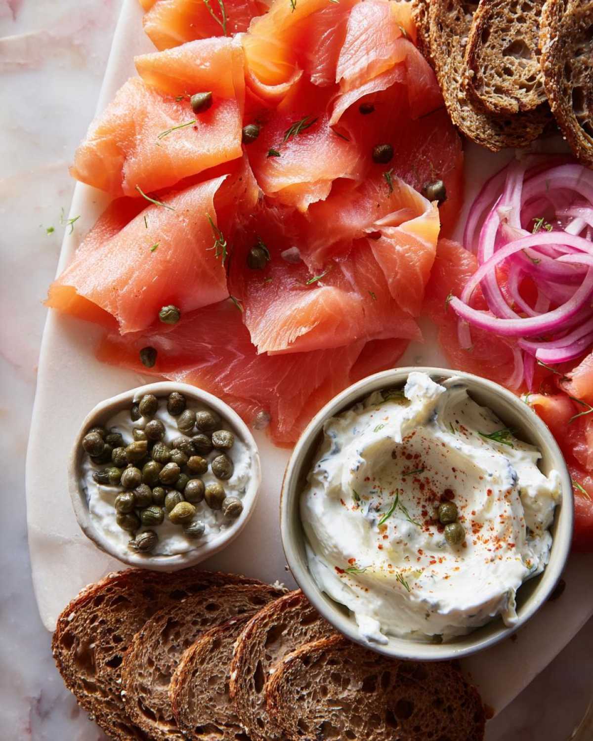 Overhead view of a Breakfast Grazing Board with Smoked Salmon, cream cheese, capers, red onion, and dark rye bread slices.